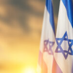 Israel flags with a star of David over cloudy sky background on sunset.
